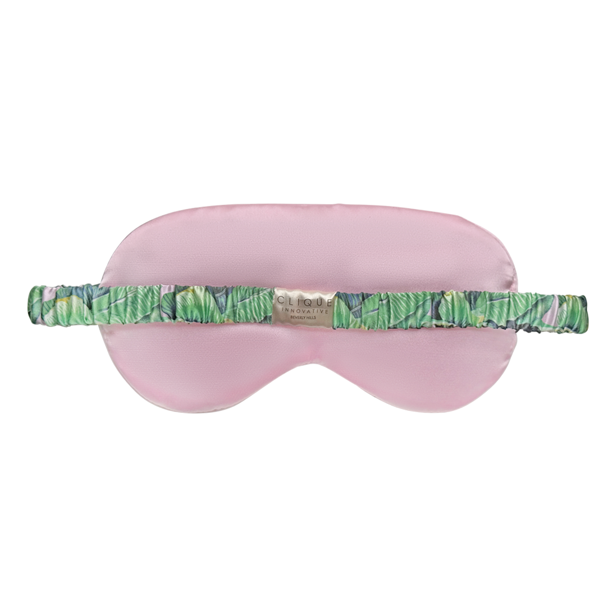 Back view of a pink satin sleep eye mask with a green tropical leaf–print elastic strap and a small “Clique Innovative Beverly Hills” brand label at the center, shown on a white background.