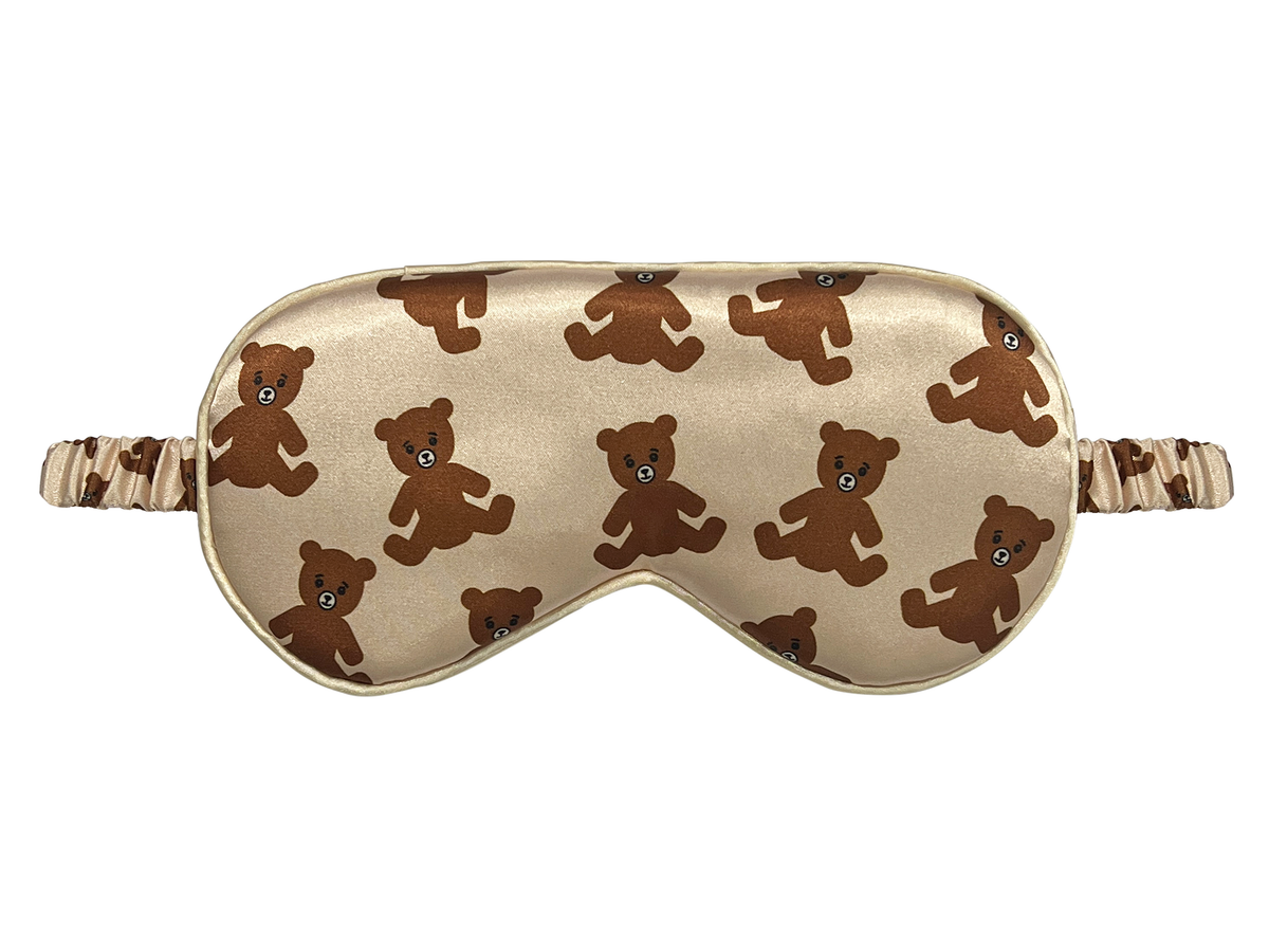 Front view of a beige satin eye mask with an all-over brown teddy bear print.