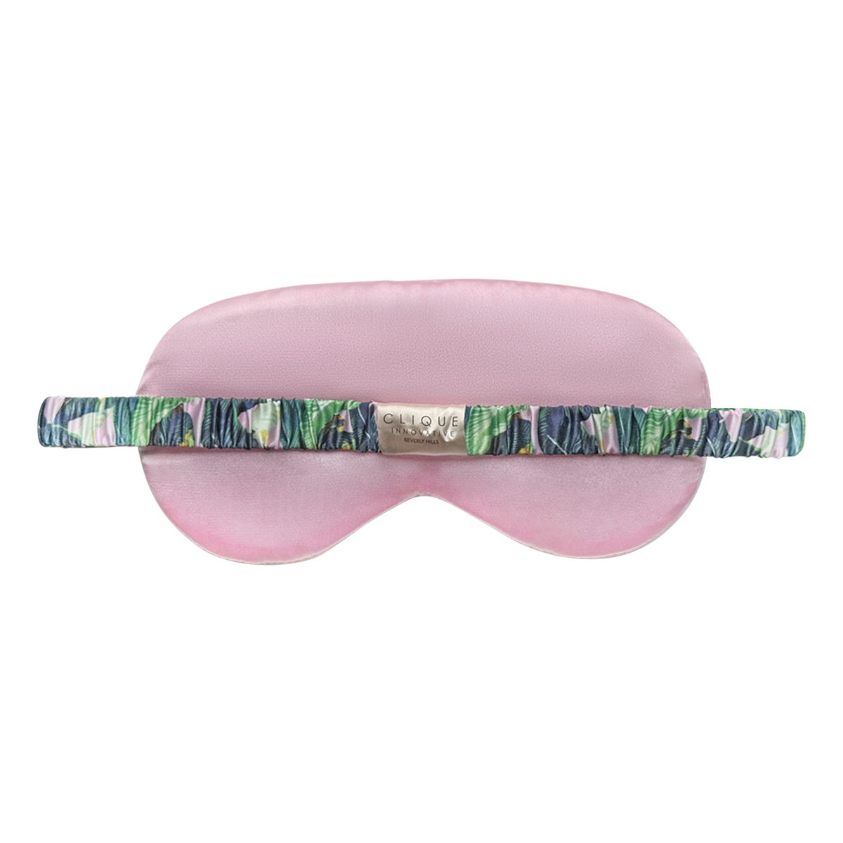 Back view of a pink satin sleep eye mask with a tropical leaf–print ruched elastic strap and a small gold “Clique Innovative Beverly Hills” brand label, shown on a white background.