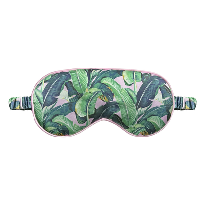 Front view of a tropical banana leaf satin sleep eye mask with soft pink trim and ruched elastic strap, displayed on a white background.