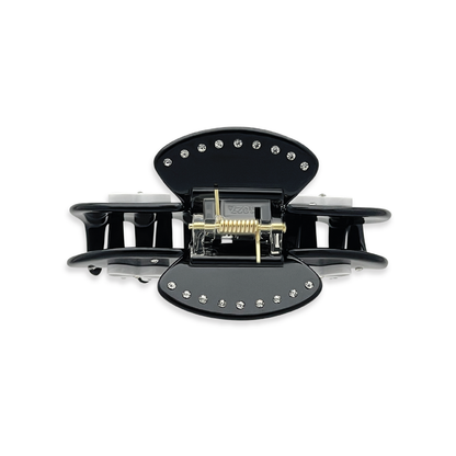 Top view of a black claw clip with silver rhinestones outlining the top edges and a visible gold spring mechanism on a white background.