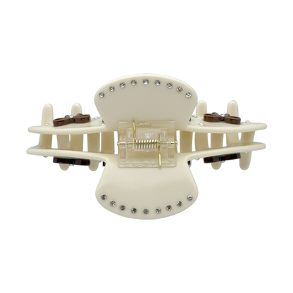 Top view of a beige bow claw clip showing the spring and rhinestone details
