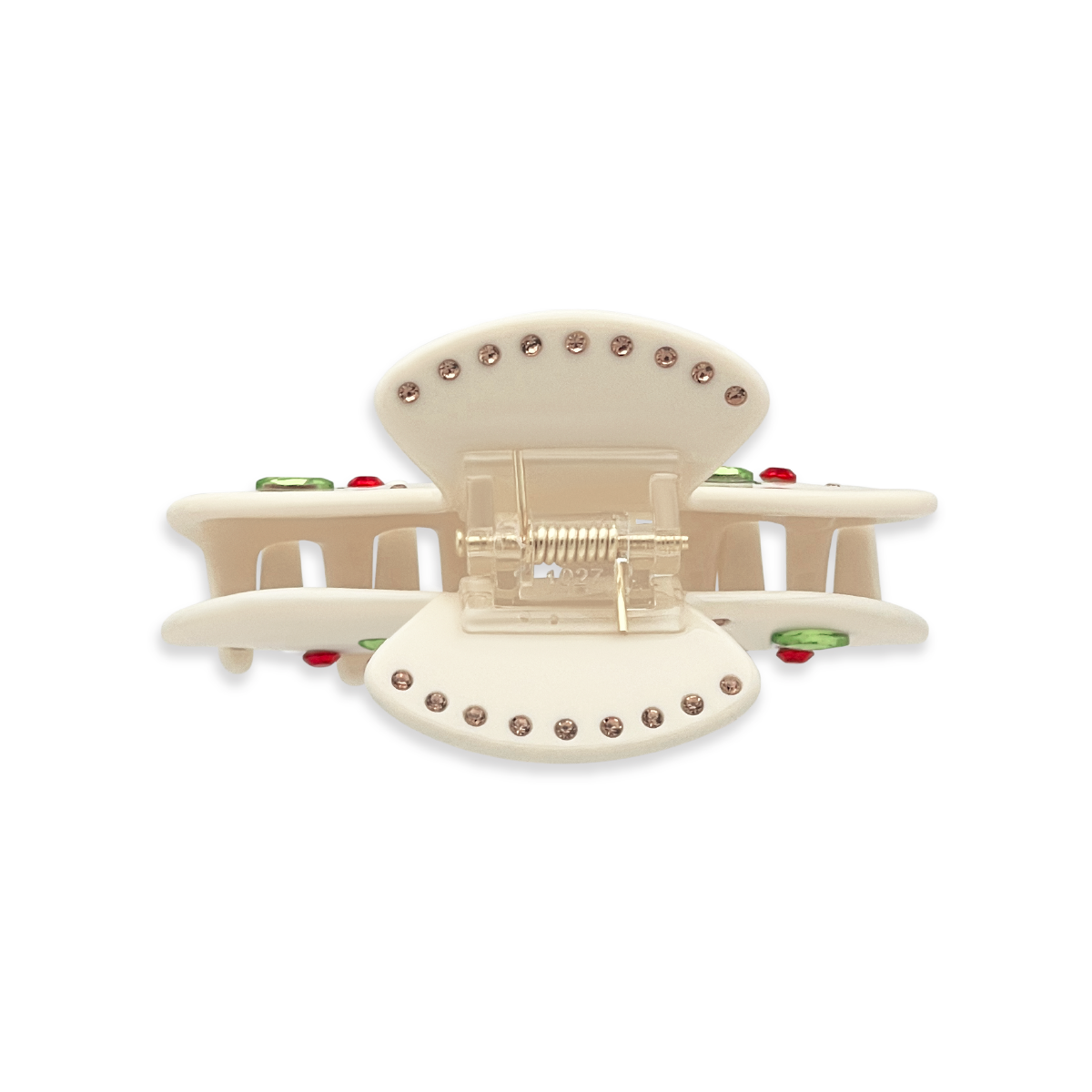 Top view of a beige claw clip showing gold rhinestones along the top edges, a gold spring mechanism, and glimpses of green leaf rhinestones and red cherry details on a white background.