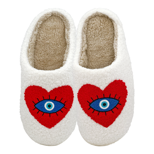 Pair of white fuzzy slippers with embroidered red heart shapes featuring blue evil eye designs on a white background.