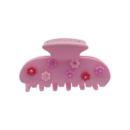 Front view of a blush pink claw clip decorated with multiple small flower-shaped graphics and silver rhinestone centers at the top of the claw clip on a white background.