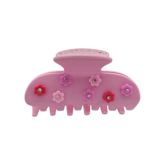 Front view of a blush pink claw clip decorated with multiple small flower-shaped graphics and silver rhinestone centers at the top of the claw clip on a white background.