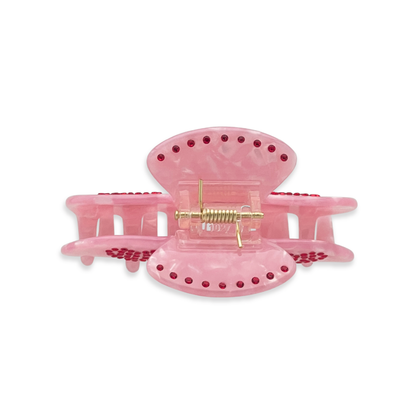 Top view of a pink marble claw clip with red rhinestone accents arranged along the edges on a white background.