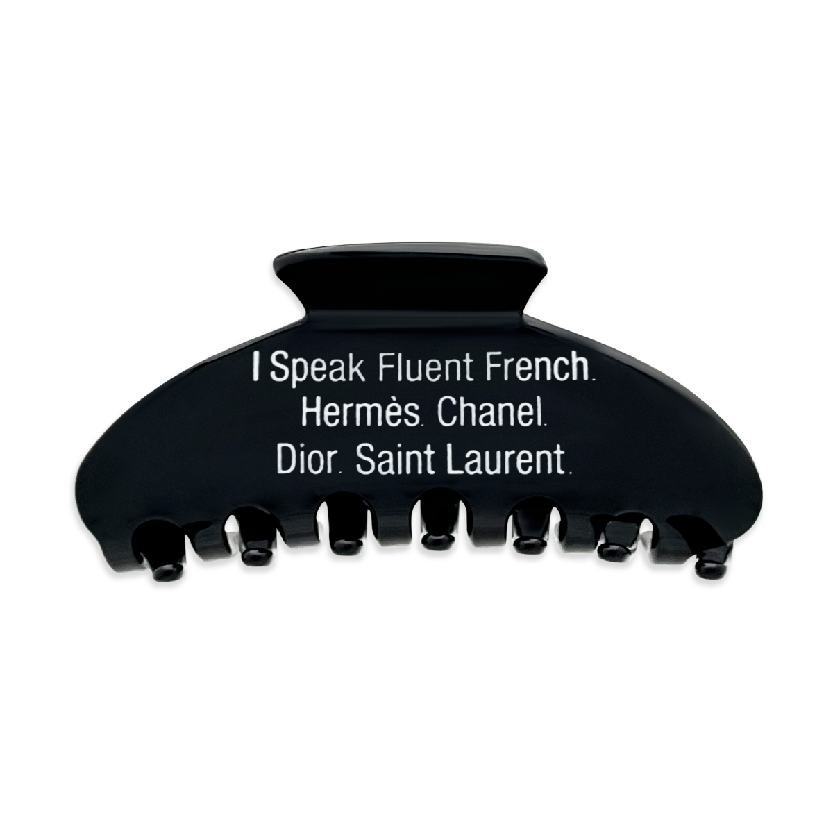 Front view of a black claw clip with white text that reads “I Speak Fluent French. Hermès. Chanel. Dior. Saint Laurent" on a white background.