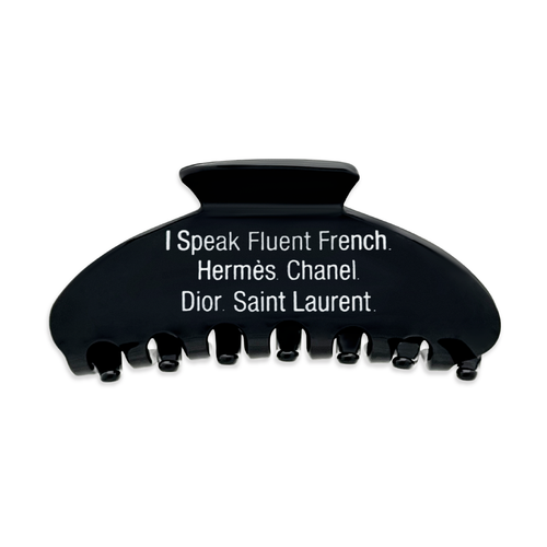Front view of a black claw clip with white text that reads “I Speak Fluent French. Hermès. Chanel. Dior. Saint Laurent" on a white background.