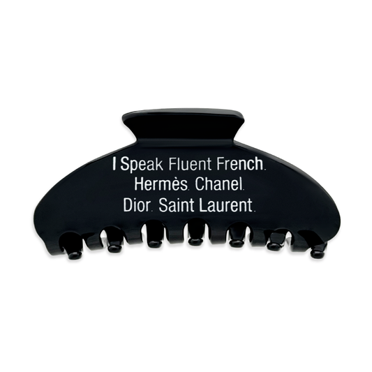 Front view of a black claw clip with white text that reads “I Speak Fluent French. Hermès. Chanel. Dior. Saint Laurent" on a white background.