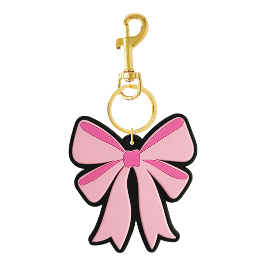 Pink bow bag charm with a gold clasp and branded gold key ring reading “Clique Innovative Beverly Hills,” shown on a white background.