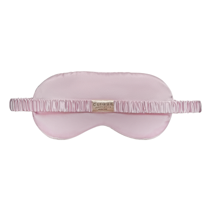 Back view of a light pink satin sleep eye mask with a ruched matching strap and a small “Clique Innovative Beverly Hills” tag at the center, shown on a white background.